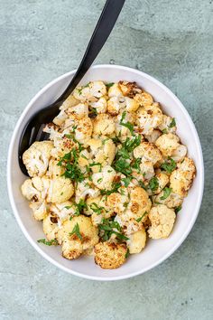 a white bowl filled with cauliflower on top of a blue tablecloth next to a black spoon