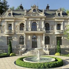 a large white building with a fountain in front of it and lots of greenery