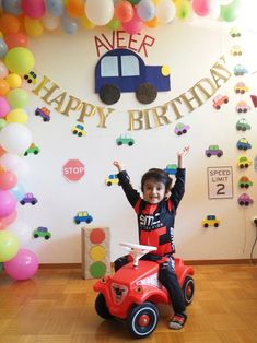 a young boy sitting on top of a toy car in front of a birthday sign