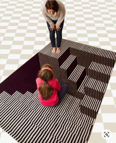 two children are sitting on a black and white checkered area rug, looking down at the floor