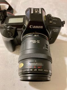 a canon camera sitting on top of a bed next to a digital camera with the lens attached