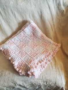 a pink crocheted blanket sitting on top of a bed next to a pillow