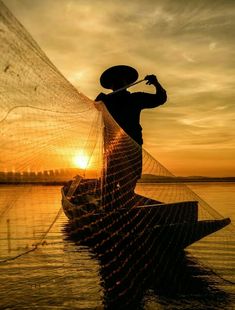 a person on a boat with a fishing net in the water at sunset or dawn