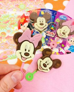 a person is holding some mickey and minnie mouse hair clips in their hand, with other disney characters on the background