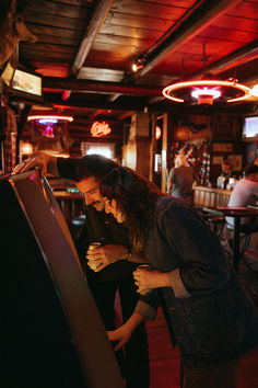 two people standing next to each other in a bar looking at something on the phone