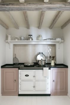 an old fashioned stove in a kitchen with pink cupboards and white appliances on the wall