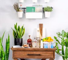 a wooden table topped with potted plants next to a wall mounted shelf filled with books