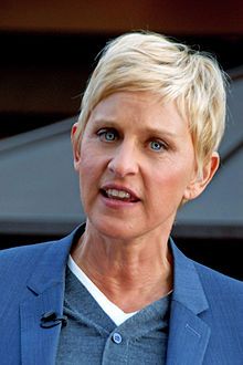 a woman with blonde hair wearing a blue jacket and gray shirt is standing in front of a building