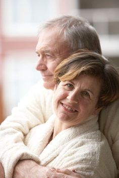 an older man and woman embracing each other while sitting on a couch in front of a window