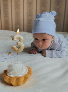 a baby laying on top of a bed next to a birthday cake with the number three candle