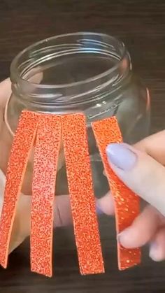 two hands are holding orange glittered strips in a mason jar with the lid open