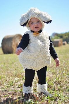 a baby wearing a sheep costume standing in the grass