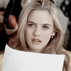 a woman holding a piece of paper in front of her face and looking at the camera