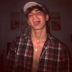 a young man making a silly face while wearing a hat and plaid shirt with his tongue out