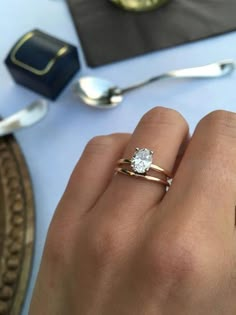 a woman's hand with a diamond ring on top of her finger next to silverware