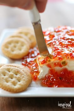 someone is cutting into some food on a white plate with crackers and crackers