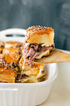 a close up of a sandwich in a white dish with a wooden spoon on the side