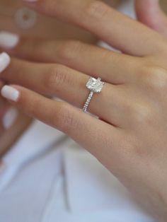 a woman's hand with a diamond ring on her finger and white manicured nails