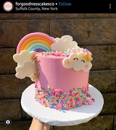 there is a pink cake with sprinkles and a rainbow on top that has a cloud