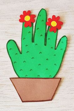 a paper cutout of a cactus with red flowers in a brown pot on a wooden surface