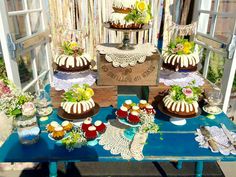 a table topped with cakes and cupcakes covered in frosting next to a window