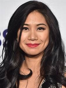 a woman with long black hair wearing a dress and red lipstick smiling at the camera