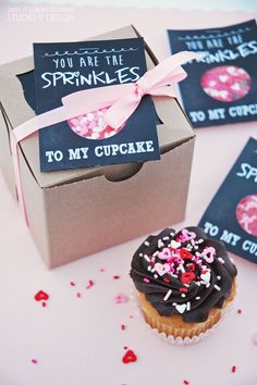 a cupcake with sprinkles is in a box next to some tags