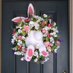 a white bunny wreath with pink flowers and greenery on the front door to a house