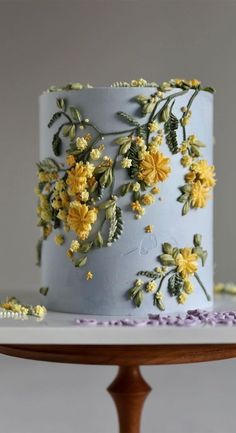 a blue cake with yellow flowers on it sitting on a wooden table next to a white plate