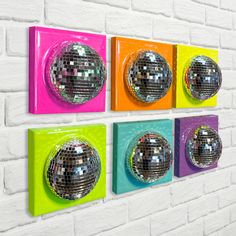 four disco balls mounted to the side of a white brick wall with multicolored tiles