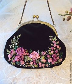 a black purse with pink roses on it sitting on a lace covered tablecloth next to flowers