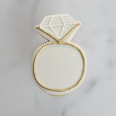 a white and gold ring with a diamond on the top, sitting on a marble surface