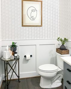 a white toilet sitting in a bathroom next to a wooden table with a potted plant on it