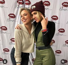 two women standing next to each other in front of a wall