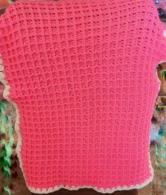 a pink crocheted blanket sitting on top of a wooden chair next to a wall