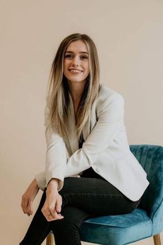 a woman sitting on top of a blue chair in front of a white wall with her legs crossed