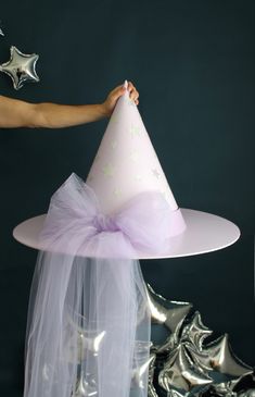 a person holding a pink party hat on top of a white cake stand with silver stars in the background