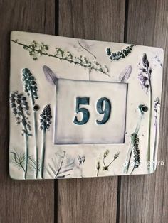 the number 59 is surrounded by flowers and leaves on a white tile plaque that reads,