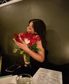 a woman sitting at a table with flowers in front of her face and writing on the wall behind her