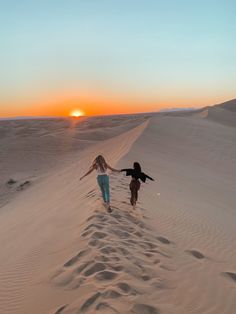 two people running across sand dunes at sunset