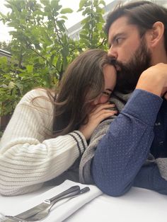 a man and woman kissing each other at a table with utensils on it