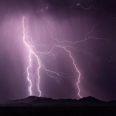 lightning strikes in the sky over mountains and hills at night with purple hues above