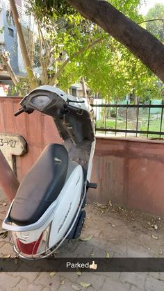 a scooter parked next to a tree in front of a fence