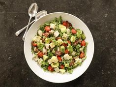 a white bowl filled with salad next to two spoons on top of a table