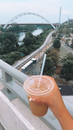 a person holding up a drink with a bridge in the background