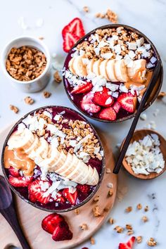 two bowls filled with fruit and granola on top of a wooden cutting board