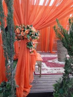 an orange wedding arch with flowers and greenery on the top, draped over it