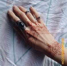 a woman's hand with henna tattoos on it and two rings in the middle