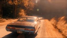 an old car driving down a dirt road next to trees and bushes in the sunlight