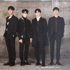 three young men standing next to each other in front of a concrete wall and wearing black suits